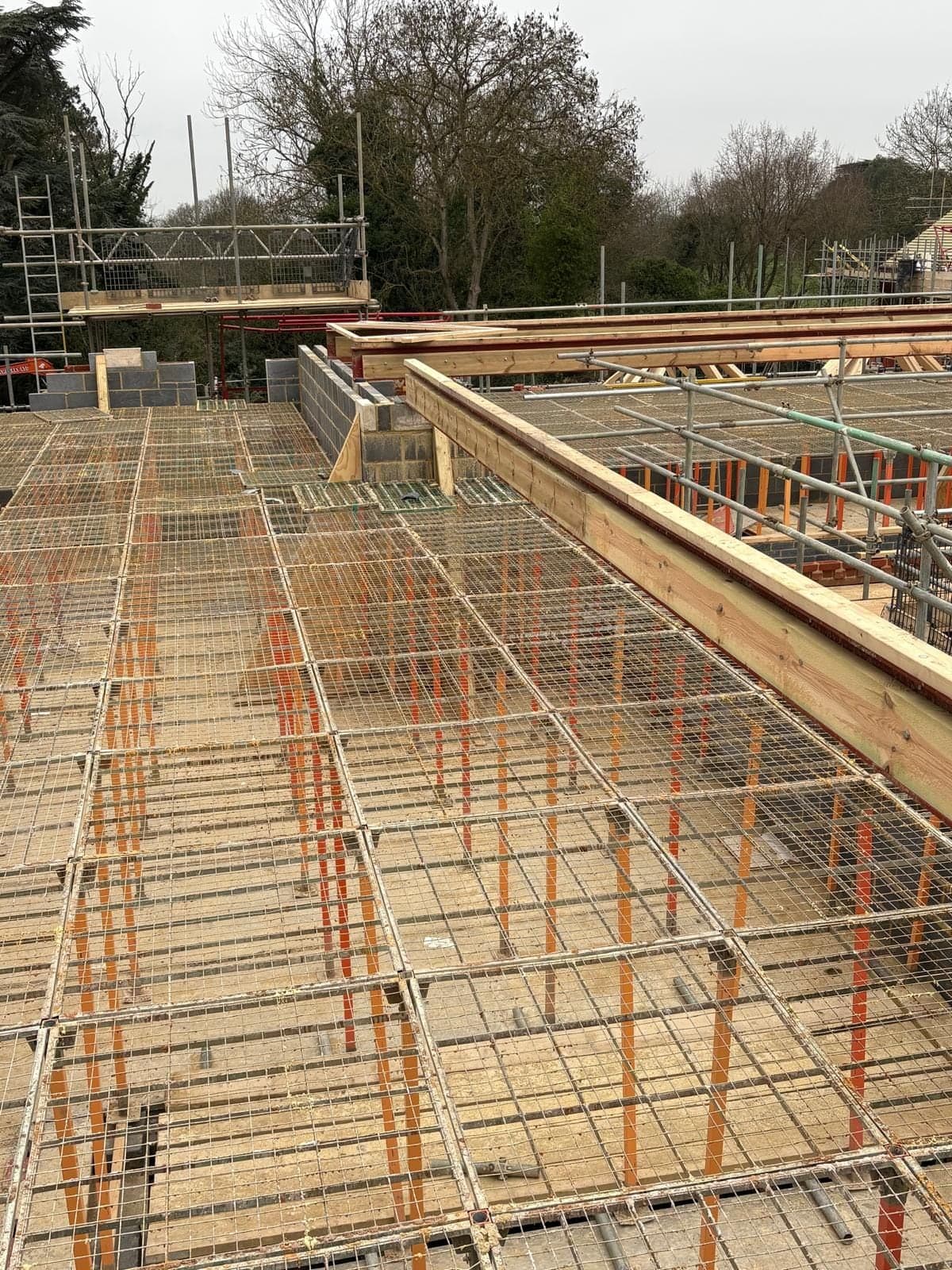 G-Deck Lite steel mesh decking on orange legs across a house plot, scaffold and trees beyond
