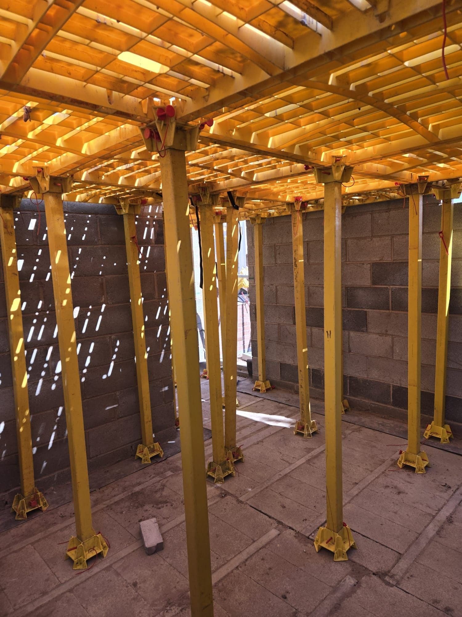 Inside a block-built room beneath a Trad Deck platform, yellow legs and sunlight through the panels